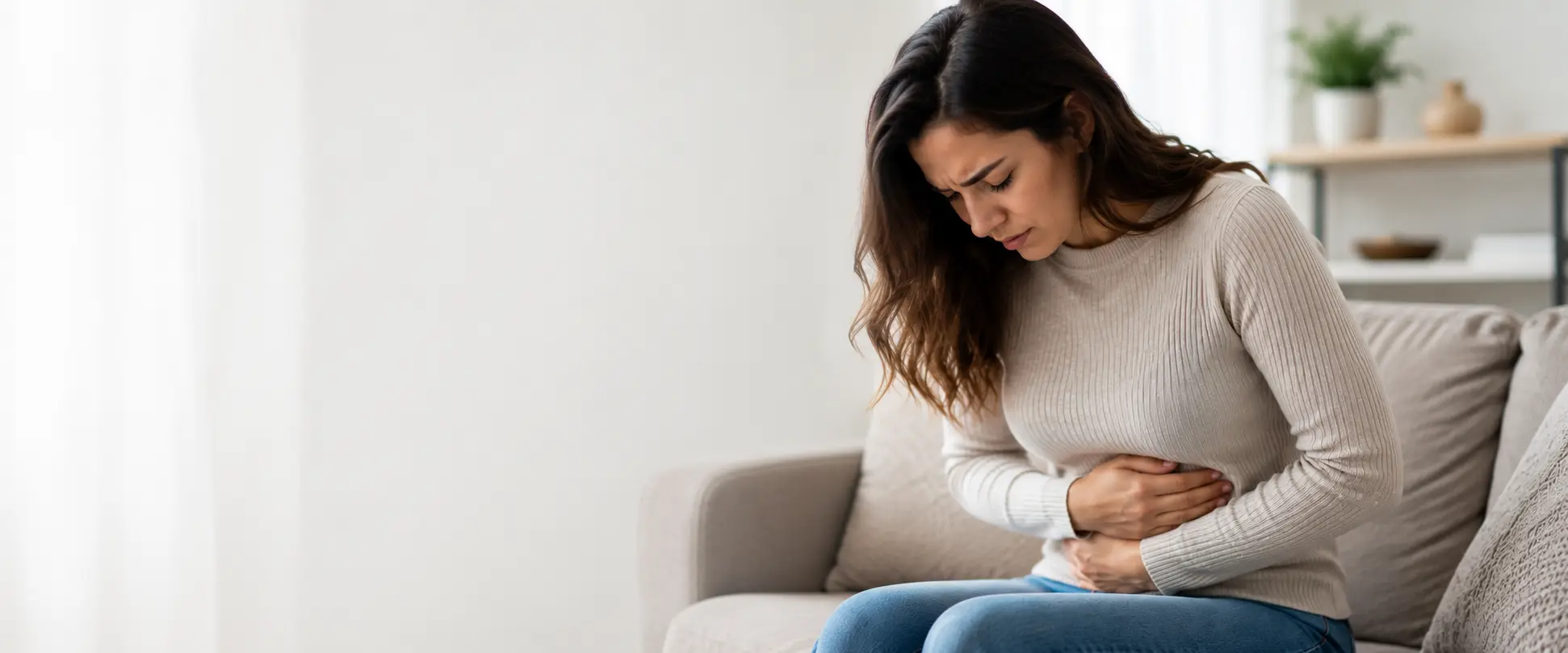 Person holding their abdomen while experiencing stomach discomfort in a home setting.