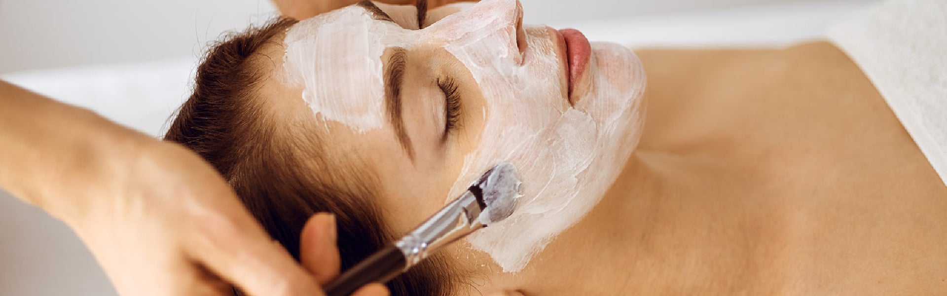 A skincare professional applying a facial mask during a professional facial treatment at an aesthetic clinic.