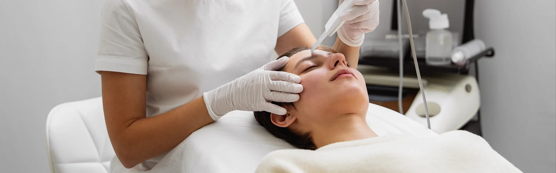 A skincare professional performing a facial treatment on a client in a modern treatment room.