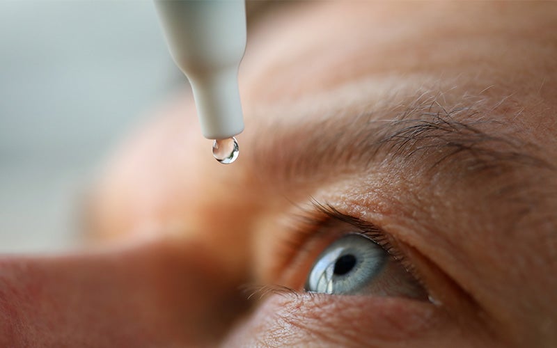 Close-up of a person's blue eye as a drop of liquid falls from an eye dropper.