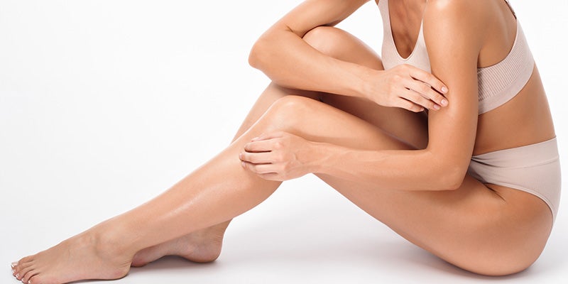 A person sitting, touching their smooth, moisturized skin on an arm and leg.